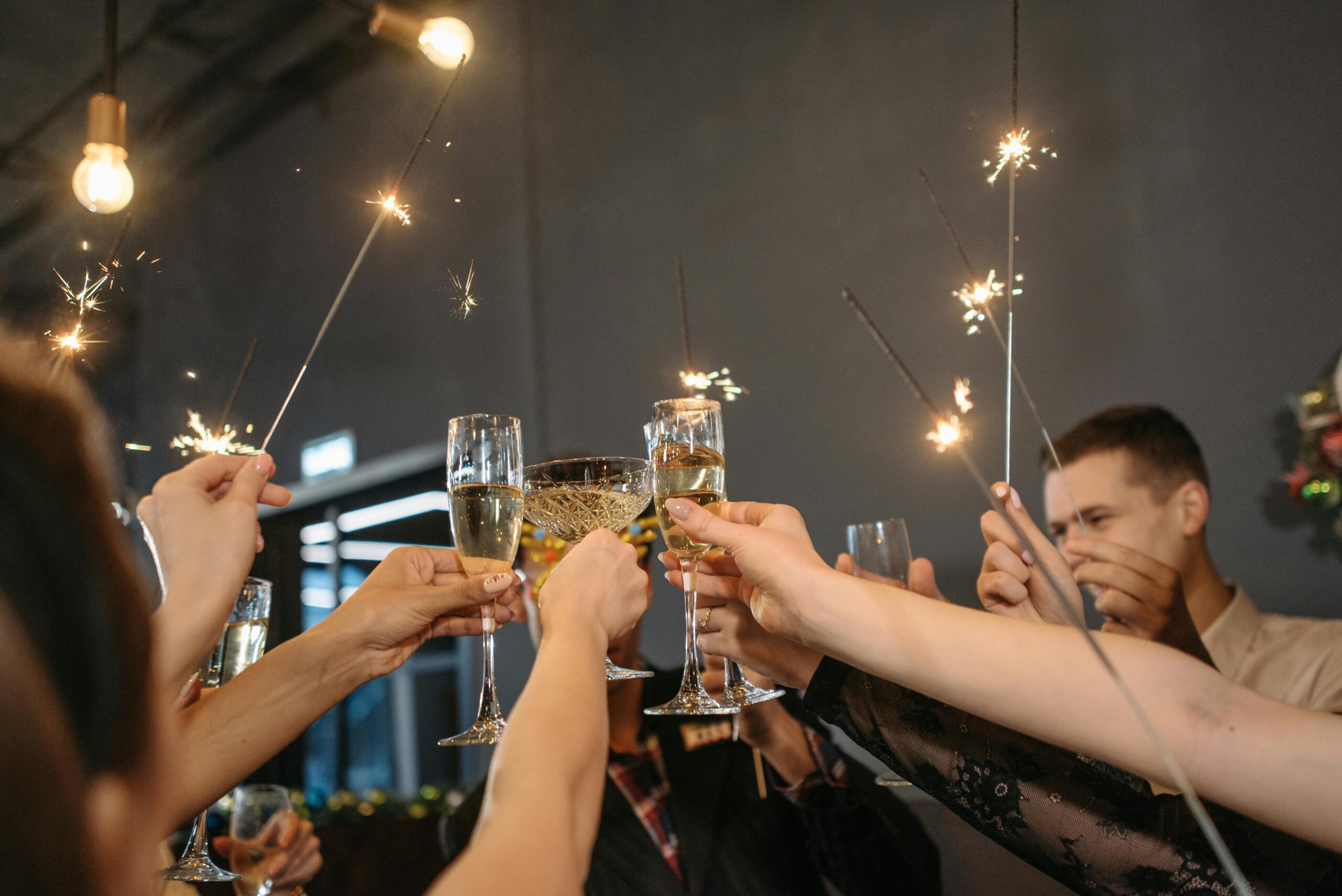 Group of adults celebrating with sparklers and toasting champagne indoors.